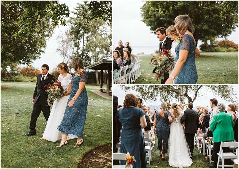 Premier Snohomish & Seattle Wedding Photographer | GSquared Weddings Photography A bride in a white dress walks down an outdoor aisle at a scenic Snohomish Seattle wedding, accompanied by two people. Guests seated on white chairs watch and smile amid lush trees and green grass. 47.9129° N, 122.0982° W | Serving Snohomish, Seattle , Orlando & Beyond