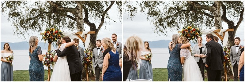 Premier Snohomish & Seattle Wedding Photographer | GSquared Weddings Photography Two side-by-side photos of a Snohomish outdoor wedding show a bride hugging a woman in a blue dress, then standing with a man in a suit beside an officiant under a floral archway near a lake, with smiling wedding party members nearby. 47.9129° N, 122.0982° W | Serving Snohomish, Seattle , Orlando & Beyond
