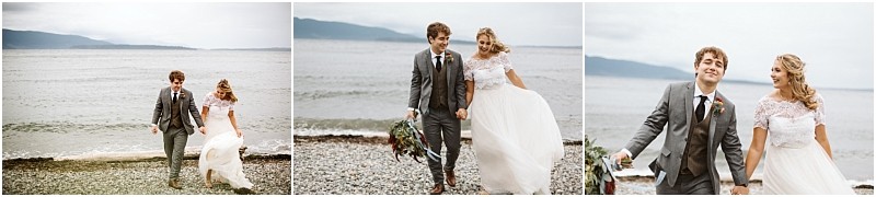 Premier Snohomish & Seattle Wedding Photographer | GSquared Weddings Photography A bride and groom walk hand in hand along a rocky beach near Snohomish, smiling and laughing together. The bride wears a white dress and the groom wears a gray suit, with calm water and mountains framing their Seattle wedding day. 47.9129° N, 122.0982° W | Serving Snohomish, Seattle , Orlando & Beyond