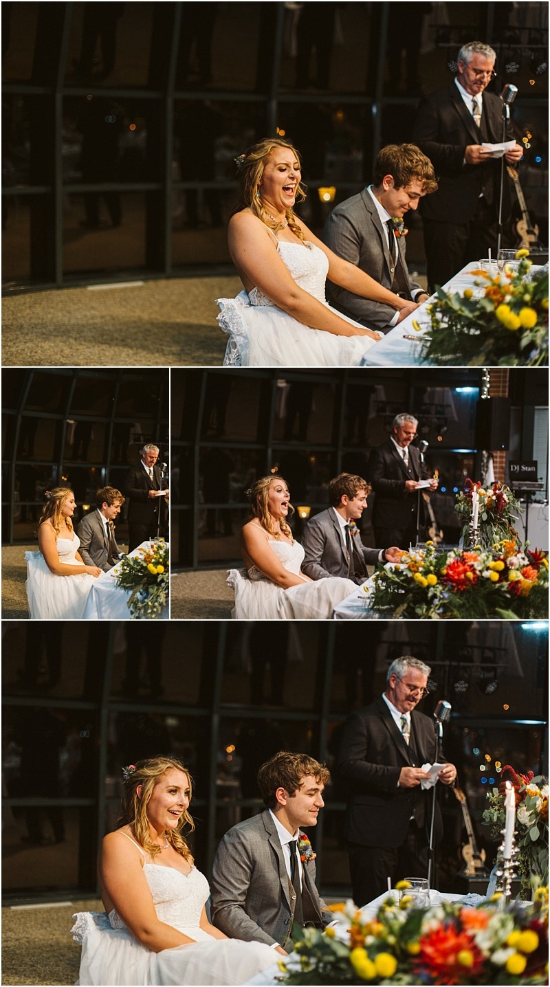 Premier Snohomish & Seattle Wedding Photographer | GSquared Weddings Photography A bride and groom sit smiling at a decorated table during their Snohomish wedding reception while an older man stands behind them, speaking into a microphone. The mood is joyful, and the room is warmly lit. 47.9129° N, 122.0982° W | Serving Snohomish, Seattle , Orlando & Beyond