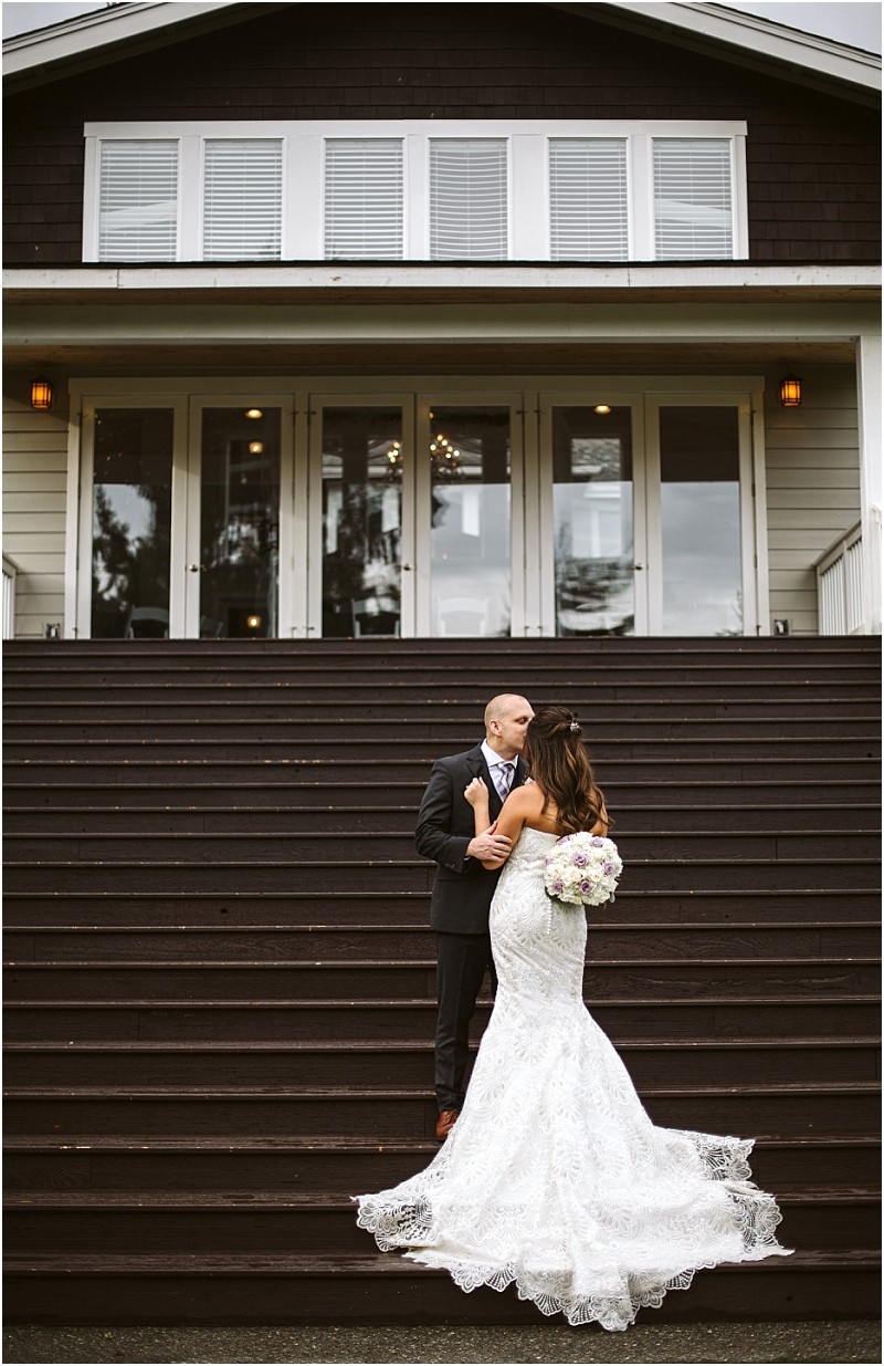 Premier Snohomish & Seattle Wedding Photographer | GSquared Weddings Photography A bride in a white lace gown holding a bouquet stands on outdoor steps, facing her groom in a dark suit. They look at each other in front of a large building with glass doors and white trim at their Snohomish Seattle wedding. 47.9129° N, 122.0982° W | Serving Snohomish, Seattle , Orlando & Beyond
