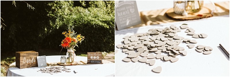Premier Snohomish & Seattle Wedding Photographer | GSquared Weddings Photography A Snohomish wedding guest book table outdoors features a wooden card box, a mason jar with orange and yellow flowers, a small sign, and scattered wooden hearts on a white tablecloth in sunlight. 47.9129° N, 122.0982° W | Serving Snohomish, Seattle , Orlando & Beyond