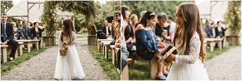 Premier Snohomish & Seattle Wedding Photographer | GSquared Weddings Photography A young flower girl in a white lace dress walks down an outdoor aisle at a Snohomish wedding, holding a wooden box, while guests watch and smile during the ceremony. 47.9129° N, 122.0982° W | Serving Snohomish, Seattle , Orlando & Beyond