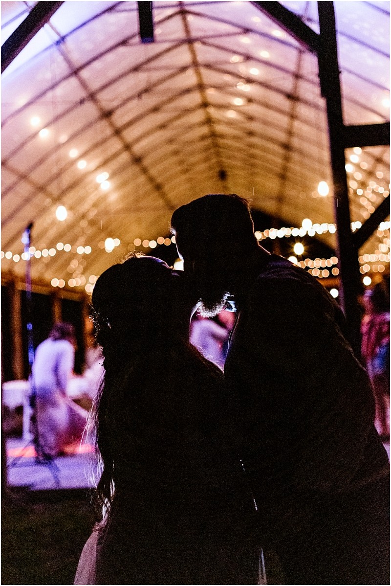 Premier Snohomish & Seattle Wedding Photographer | GSquared Weddings Photography Silhouetted couple facing each other under a transparent, arched ceiling with string lights at a Snohomish Seattle wedding engagement, surrounded by soft, warm lighting and blurred people in the background, creating a romantic atmosphere. 47.9129° N, 122.0982° W | Serving Snohomish, Seattle , Orlando & Beyond