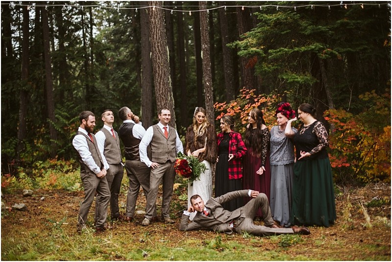 Premier Snohomish & Seattle Wedding Photographer | GSquared Weddings Photography A wedding party poses in a Snohomish forest. The bride holds a bouquet and stands with bridesmaids and groomsmen. One man lies playfully in front as the rest smile and laugh, capturing the joy of a Seattle wedding among colorful autumn trees. 47.9129° N, 122.0982° W | Serving Snohomish, Seattle , Orlando & Beyond