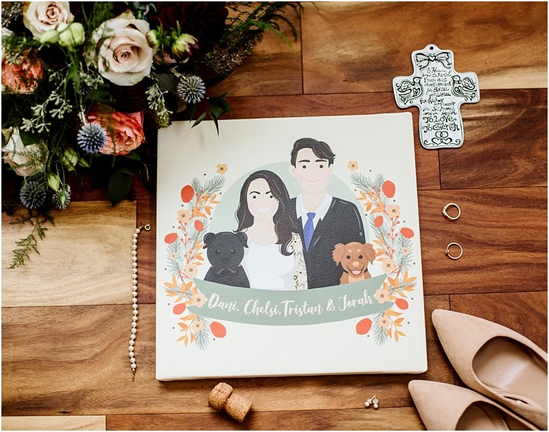 Premier Snohomish & Seattle Wedding Photographer | GSquared Weddings Photography A Snohomish Seattle wedding flat lay features a floral bouquet, an illustrated portrait of the engaged couple with their two dogs, wedding rings, a decorative cross, beige heels, and a cork on a wooden floor. The portrait reads Dani, Chels, Tristan & Jonah. 47.9129° N, 122.0982° W | Serving Snohomish, Seattle , Orlando & Beyond