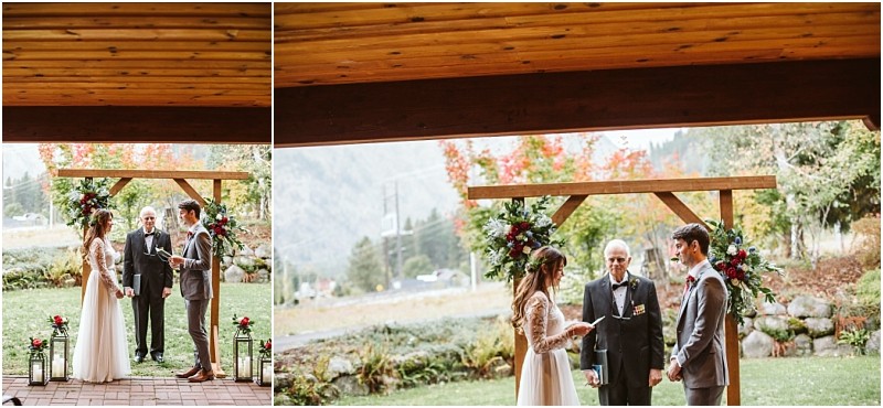 Premier Snohomish & Seattle Wedding Photographer | GSquared Weddings Photography A bride and groom stand facing each other under a wooden arch with flowers during a Snohomish outdoor wedding ceremony, with an officiant between them and mountains visible in the background. 47.9129° N, 122.0982° W | Serving Snohomish, Seattle , Orlando & Beyond