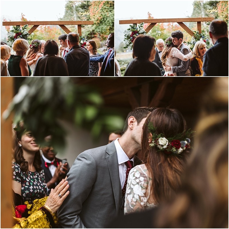 Premier Snohomish & Seattle Wedding Photographer | GSquared Weddings Photography A bride and groom kiss under a wooden archway decorated with flowers, surrounded by guests who are smiling, clapping, and celebrating their Snohomish wedding ceremony. 47.9129° N, 122.0982° W | Serving Snohomish, Seattle , Orlando & Beyond