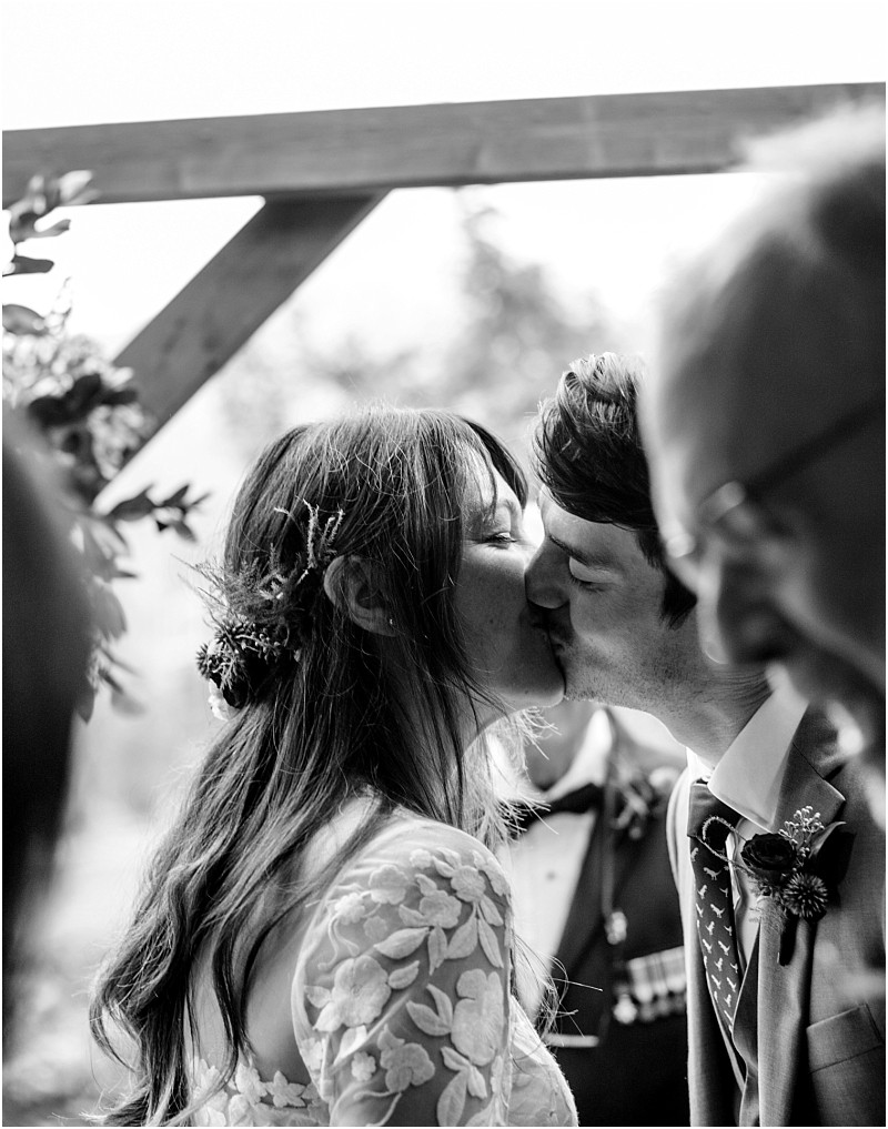 Premier Snohomish & Seattle Wedding Photographer | GSquared Weddings Photography A bride and groom share a kiss during their Snohomish wedding ceremony, surrounded by loved ones. The black and white image captures an intimate and joyful moment in the heart of Seattle’s wedding scene. 47.9129° N, 122.0982° W | Serving Snohomish, Seattle , Orlando & Beyond