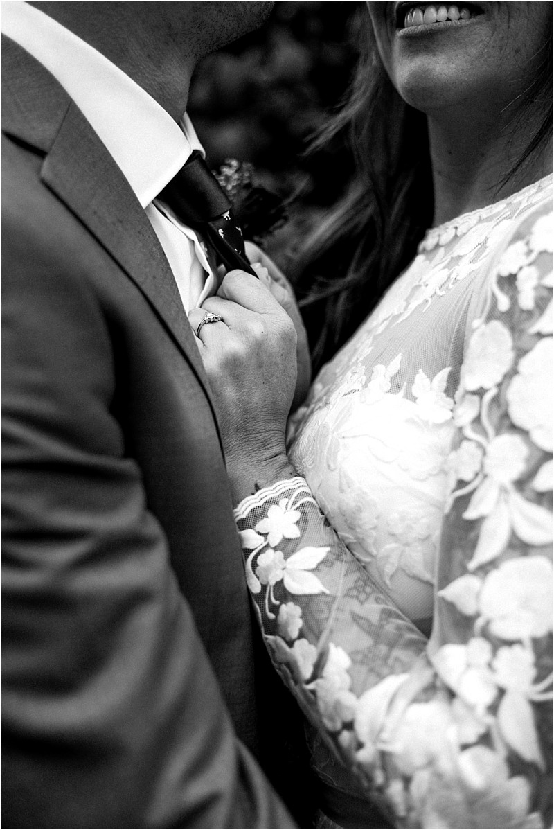Premier Snohomish & Seattle Wedding Photographer | GSquared Weddings Photography Black and white close-up of a couple in wedding attire, with the bride smiling and holding the groom’s tie. Her lace dress and engagement ring stand out. Capturing a timeless Snohomish Seattle wedding moment, their faces are mostly out of frame. 47.9129° N, 122.0982° W | Serving Snohomish, Seattle , Orlando & Beyond