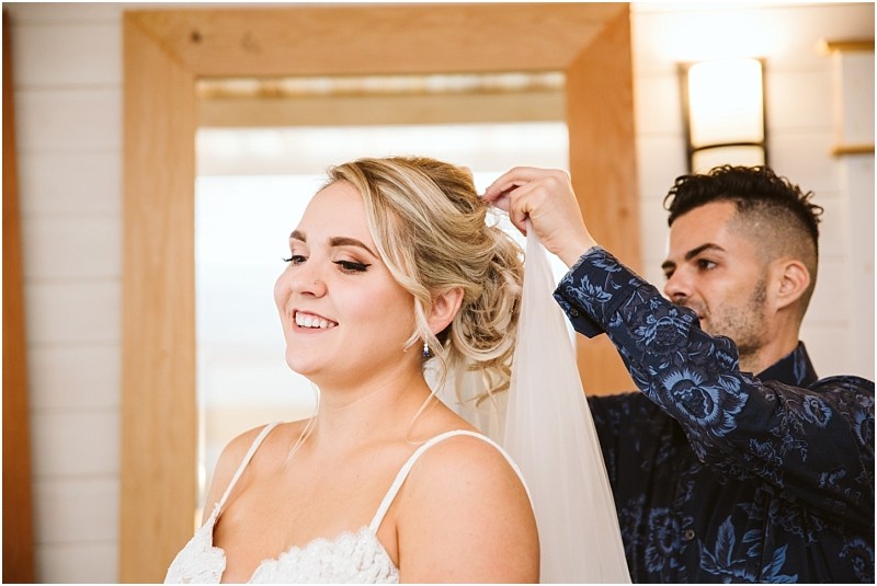 Premier Snohomish & Seattle Wedding Photographer | GSquared Weddings Photography A smiling bride in a white dress has her veil adjusted by a person behind her in a blue patterned shirt, inside a brightly lit room with wooden accents—a joyful moment from a Snohomish Seattle wedding engagement. 47.9129° N, 122.0982° W | Serving Snohomish, Seattle , Orlando & Beyond