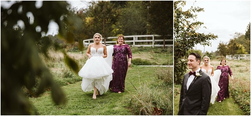 Premier Snohomish & Seattle Wedding Photographer | GSquared Weddings Photography A bride in a white gown walks barefoot on a grassy path at a Snohomish wedding, holding her dress, with a woman in a purple dress behind her. A man in a tuxedo stands ahead; trees and a white fence are in the background. 47.9129° N, 122.0982° W | Serving Snohomish, Seattle , Orlando & Beyond