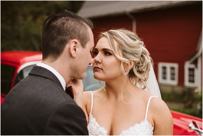 Premier Snohomish & Seattle Wedding Photographer | GSquared Weddings Photography A bride and groom stand close together outdoors, gazing into each other’s eyes. The bride gently touches the groom’s face. A red vintage car and a red barn set the scene for this charming Snohomish wedding moment. 47.9129° N, 122.0982° W | Serving Snohomish, Seattle , Orlando & Beyond