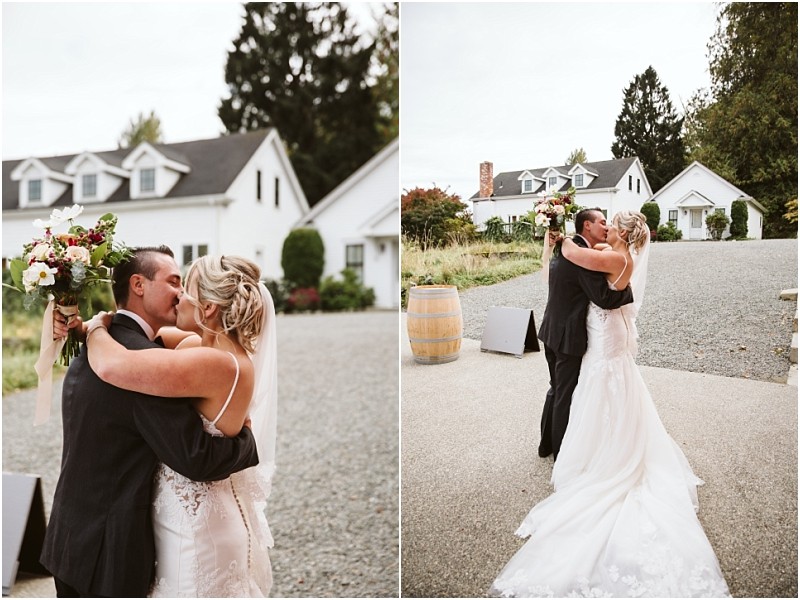 Premier Snohomish & Seattle Wedding Photographer | GSquared Weddings Photography A bride and groom embrace and kiss outdoors on their Snohomish wedding day, surrounded by white houses and greenery. The bride holds a bouquet of flowers while wearing a white gown and veil. 47.9129° N, 122.0982° W | Serving Snohomish, Seattle , Orlando & Beyond