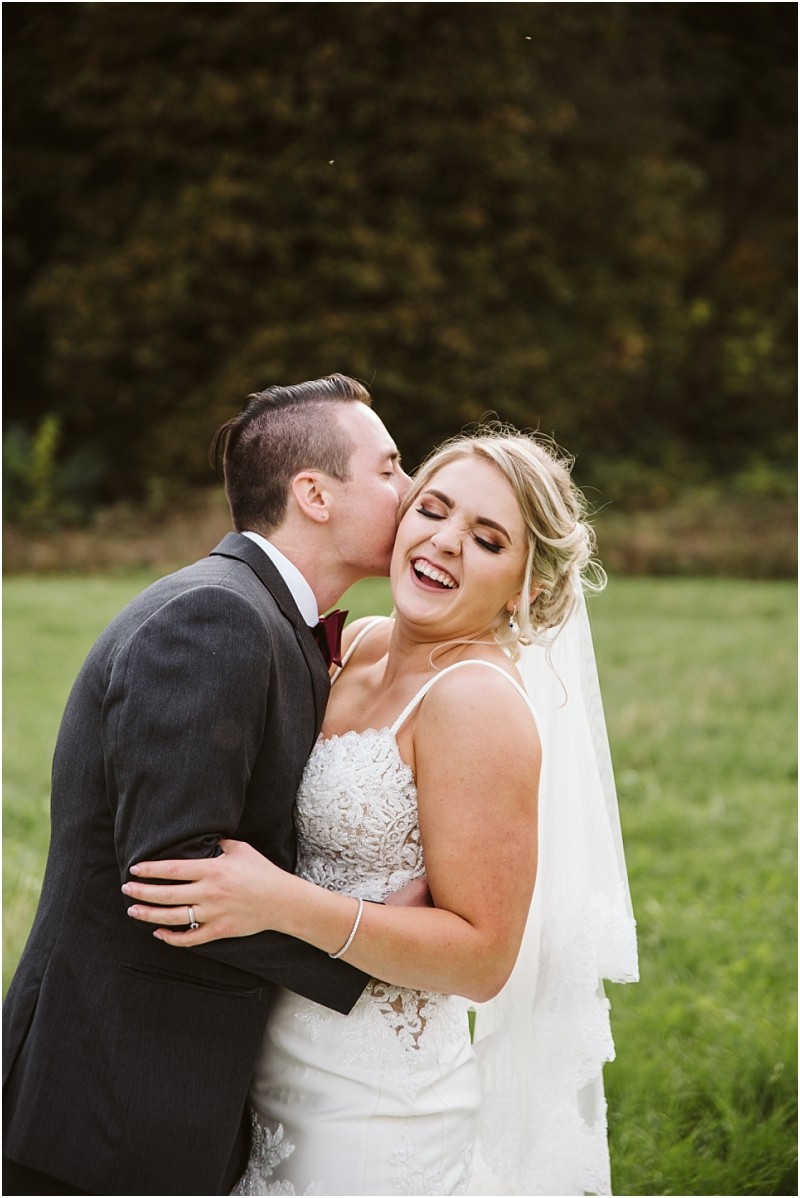 Premier Snohomish & Seattle Wedding Photographer | GSquared Weddings Photography A groom in a dark suit kisses his smiling bride on the cheek as they embrace outdoors in a green field, capturing the joy of their Snohomish Seattle wedding. The bride glows in a white lace dress and veil. 47.9129° N, 122.0982° W | Serving Snohomish, Seattle , Orlando & Beyond