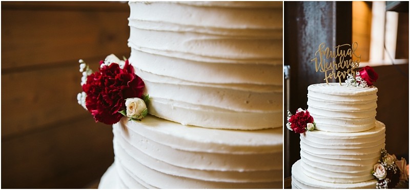 Premier Snohomish & Seattle Wedding Photographer | GSquared Weddings Photography A white, three-tiered wedding cake with textured icing, decorated with red and white flowers and a gold “Mutual Weirdness Forever” topper, displayed in a rustic wooden setting for a Snohomish Seattle wedding. 47.9129° N, 122.0982° W | Serving Snohomish, Seattle , Orlando & Beyond