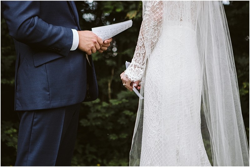 Premier Snohomish & Seattle Wedding Photographer | GSquared Weddings Photography A bride and groom stand facing each other outdoors at their Snohomish wedding, holding handwritten vows. The groom wears a dark suit, and the bride wears a lace wedding dress with a veil. Their faces are not visible. 47.9129° N, 122.0982° W | Serving Snohomish, Seattle , Orlando & Beyond