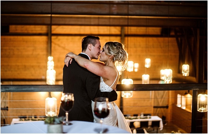 Premier Snohomish & Seattle Wedding Photographer | GSquared Weddings Photography A bride and groom embrace and share an intimate moment on a balcony at their Snohomish wedding, surrounded by warm hanging lights and soft, romantic ambiance. A table with wine glasses is in the foreground. 47.9129° N, 122.0982° W | Serving Snohomish, Seattle , Orlando & Beyond