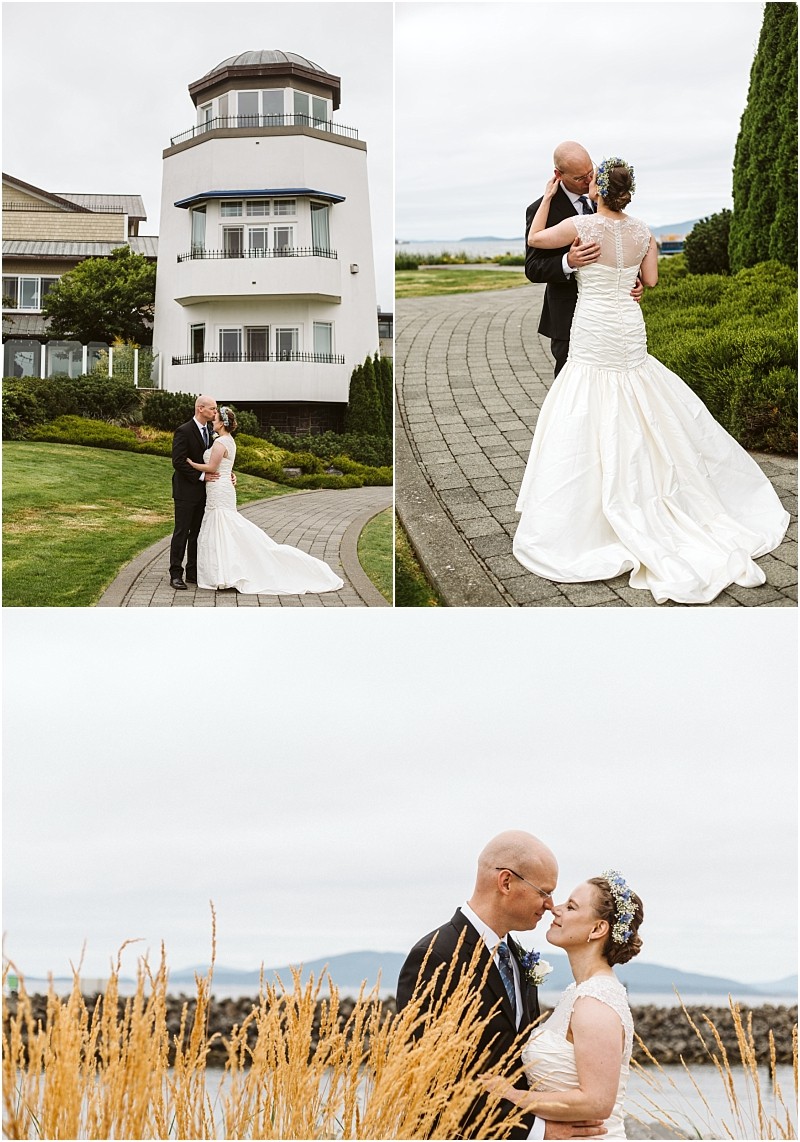 Premier Snohomish & Seattle Wedding Photographer | GSquared Weddings Photography A bride and groom, dressed formally, embrace and pose for photos outside a white lighthouse-style building near Snohomish, on a curving walkway and by tall grass with water and mountains in the background. 47.9129° N, 122.0982° W | Serving Snohomish, Seattle , Orlando & Beyond