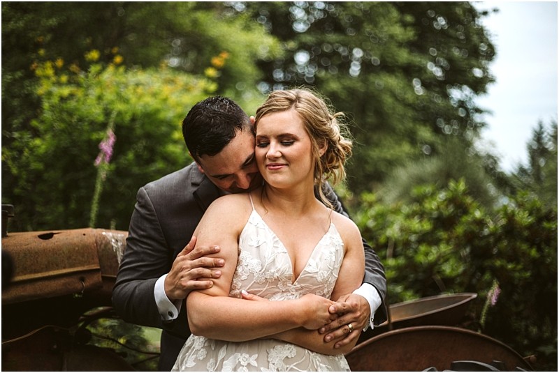 Premier Snohomish & Seattle Wedding Photographer | GSquared Weddings Photography A bride and groom embrace outdoors during their Snohomish Seattle wedding. The groom, in a dark suit, gently holds his bride in her white lace dress as lush greenery surrounds them, capturing an intimate engagement moment. 47.9129° N, 122.0982° W | Serving Snohomish, Seattle , Orlando & Beyond