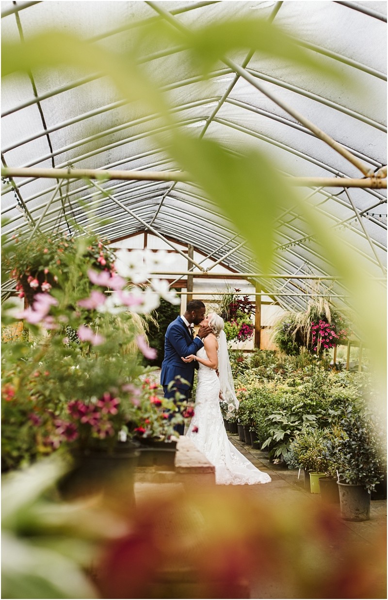 Premier Snohomish & Seattle Wedding Photographer | GSquared Weddings Photography A bride and groom share a kiss in a greenhouse full of flowers and greenery, framed by leaves and hanging plants, under a curved translucent roof during their romantic Snohomish Seattle wedding. 47.9129° N, 122.0982° W | Serving Snohomish, Seattle , Orlando & Beyond