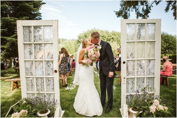barn at holly farm bothell ceremony outdoors with barn doors in the summer with blush pink bouquet bride and groom kissing