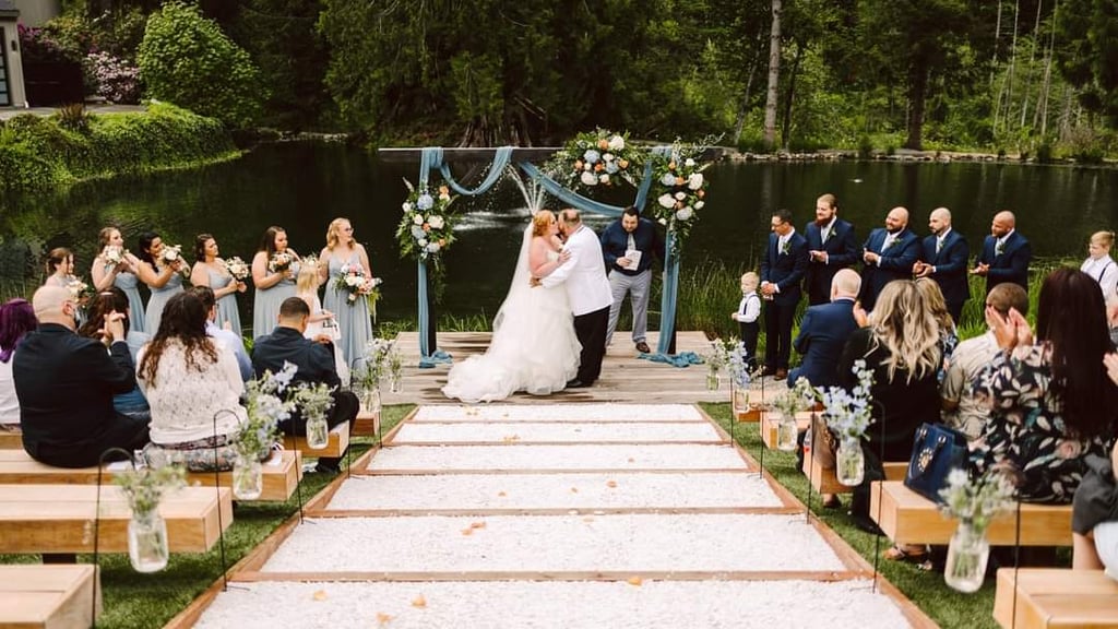 A bride and groom kiss at an outdoor lakeside wedding ceremonyone of the most picturesque Seattle wedding venuessurrounded by their wedding party seated guests on wooden benches floral decorations and lush greenery in the background Snohomish Wedding Photography A bride and groom kiss at an outdoor lakeside wedding ceremonyone of the most picturesque Seattle wedding venuessurrounded by their wedding party seated guests on wooden benches floral decorations and lush greenery in the background Snohomish Wedding Photography