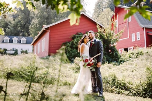 A bride and groom stand together outdoors in front of a large red barn surrounded by greenery Perfect for Washington weddings the couple smiles in wedding attire under natural sunlight as the bride holds a bouquet of flowers Snohomish Wedding Photography A bride and groom stand together outdoors in front of a large red barn surrounded by greenery Perfect for Washington weddings the couple smiles in wedding attire under natural sunlight as the bride holds a bouquet of flowers Snohomish Wedding Photography