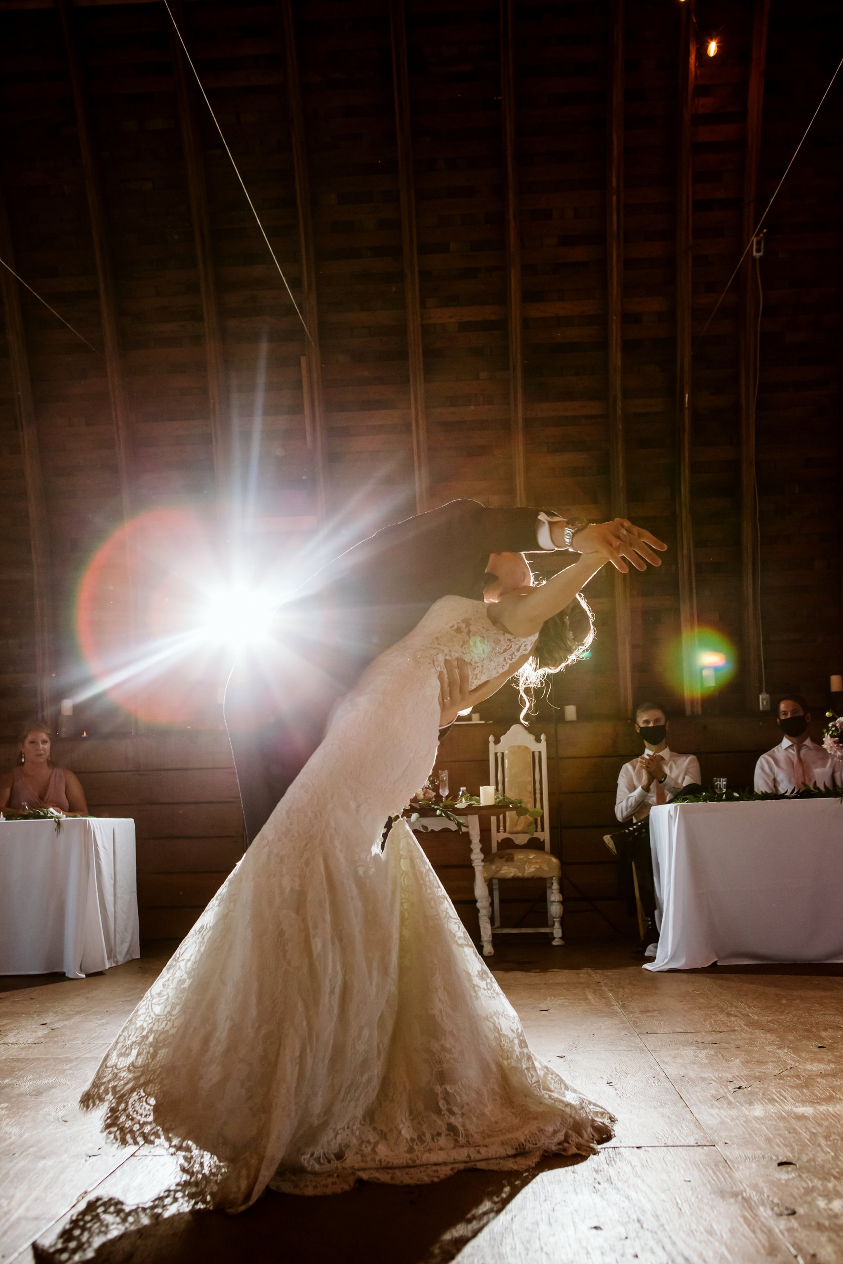 bride and groom dancing at reception with guests wearing a mask