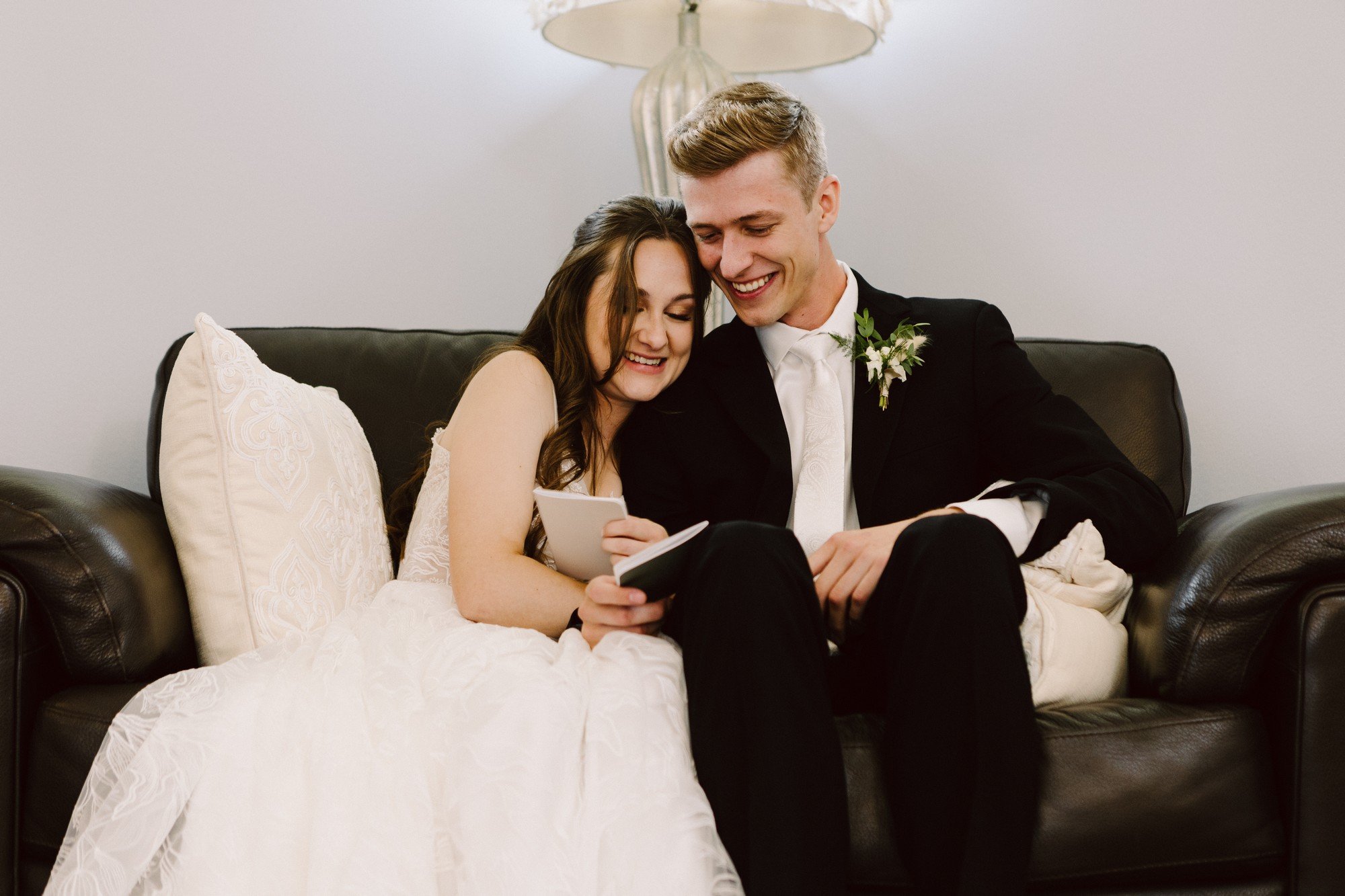 bride and groom in a room on a couch snuggled together with their vow books taking a few private moments to read their vows to eachother before the ceremony