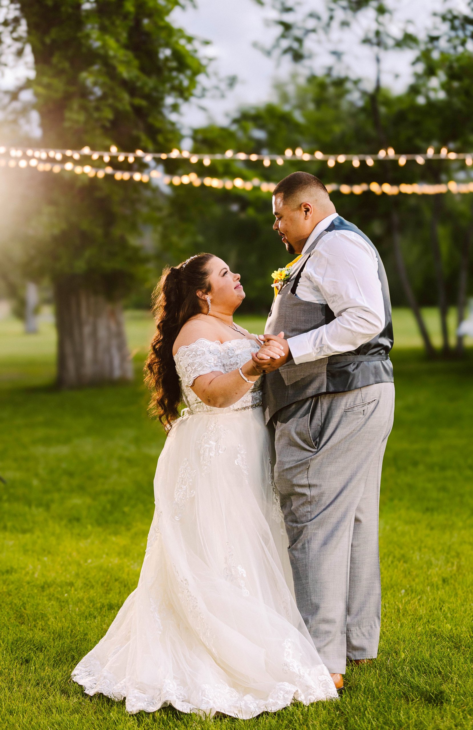 Snohomish Seattle Wedding Photographer | GSquared Weddings Photography A bride and groom share a joyful first dance outdoors under string lights surrounded by green grass and trees The bride wears a white lace dress and the groom is in a gray suit vest with no shoes 479129° N 1220982° W | Candid wedding photo by GSquared Weddings Snohomish & Seattle Wedding Photographer | GSquared Weddings Photography A bride and groom share a joyful first dance outdoors under string lights surrounded by green grass and trees The bride wears a white lace dress and the groom is in a gray suit vest with no shoes 479129° N 1220982° W | Candid wedding photo by GSquared Weddings