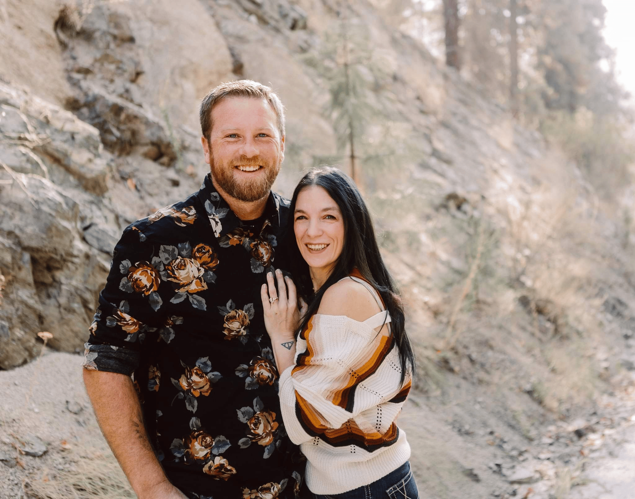 Premier Snohomish & Seattle Wedding Photographer | GSquared Weddings Photography A smiling man and woman stand close together outdoors by a rocky hillside Captured in a Seattle Snohomish Wedding Photography style the man wears a dark floral shirt while the woman in a striped sweater rests her hand on his chest Both appear happy 479129° N 1220982° W | Candid wedding photo by GSquared Weddings
