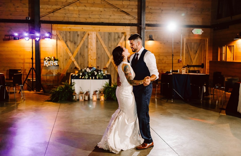 A bride and groom share a first dance in a warmly lit barn venue smiling at each other The bride wears a white dress and the groom a vest and tie Decor includes plants lanterns and a Mrs sign in the background Snohomish Wedding Photography A bride and groom share a first dance in a warmly lit barn venue smiling at each other The bride wears a white dress and the groom a vest and tie Decor includes plants lanterns and a Mrs sign in the background Snohomish Wedding Photography