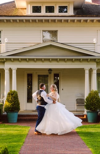 A bride and groom dance joyfully together outside a large white house with columns surrounded by green lawns and potted shrubs in warm sunlight Snohomish Wedding Photography A bride and groom dance joyfully together outside a large white house with columns surrounded by green lawns and potted shrubs in warm sunlight Snohomish Wedding Photography