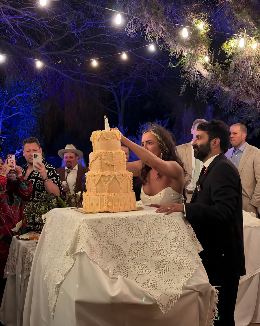 Couple cutting into tiered wedding cake under twinkling string lights