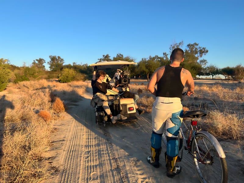 Film crew on golf cart with actor on bicycle in desert