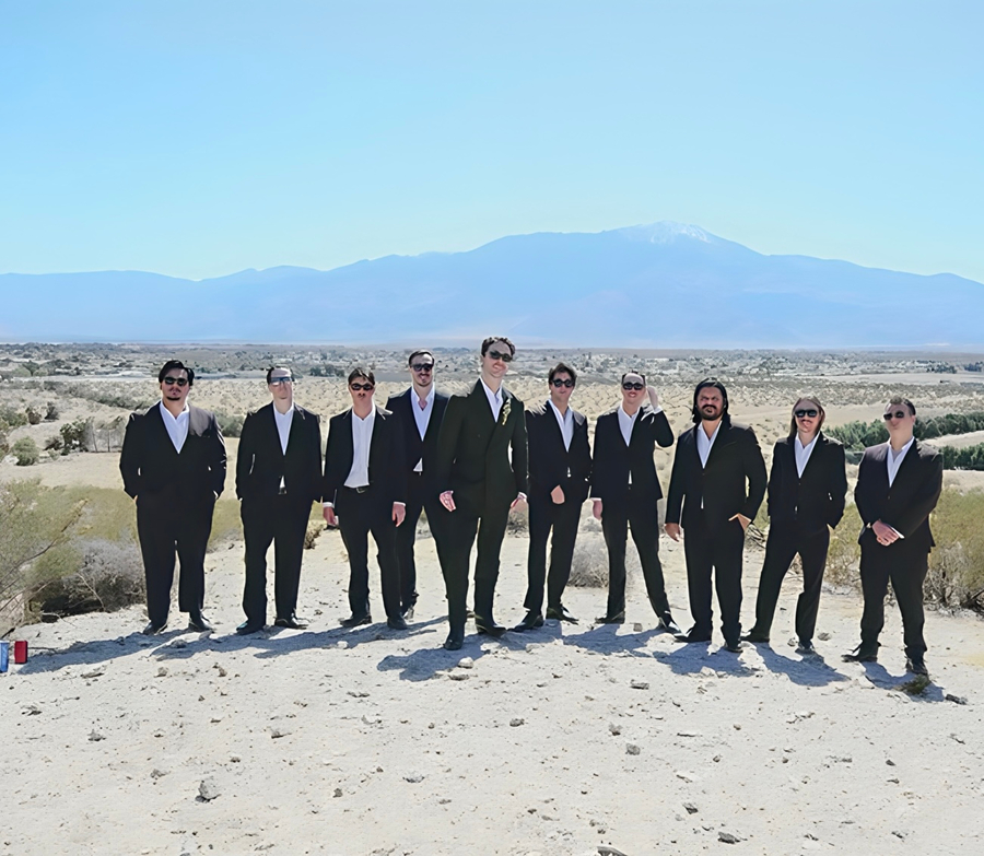 Groomsmen in all black suits lined up on the desert bluff with mountain views