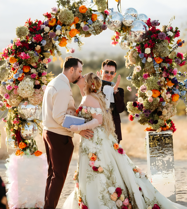 Bride and groom sharing first kiss under colorful floral arch at Bubbling Wells Oasis desert wedding