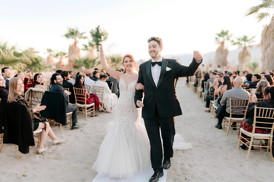 Newlyweds raising hands in celebration as they recess down the aisle at Desert Hot Springs