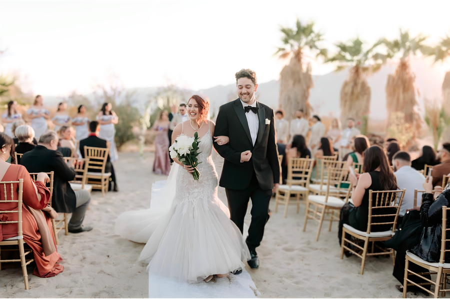 Bride and groom walking down the sandy aisle surrounded by cheering guests at Bubbling Wells Oasis