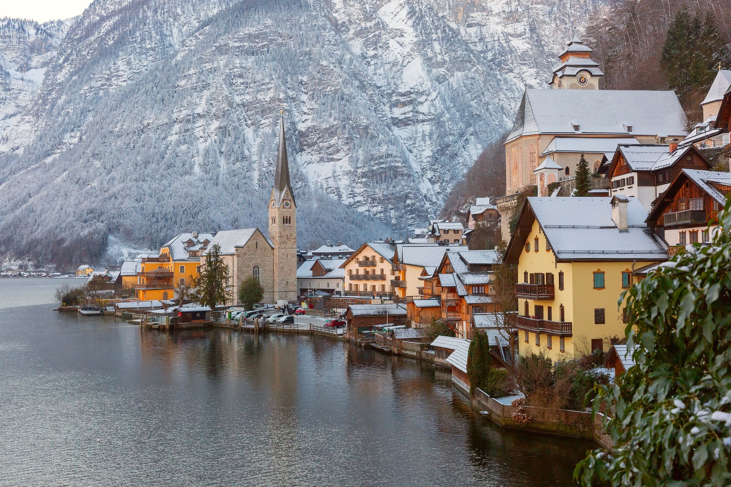 Desa Hallstatt di tepi danau Alpen yang bersalju dengan menara gereja dan pegunungan di belakangnya