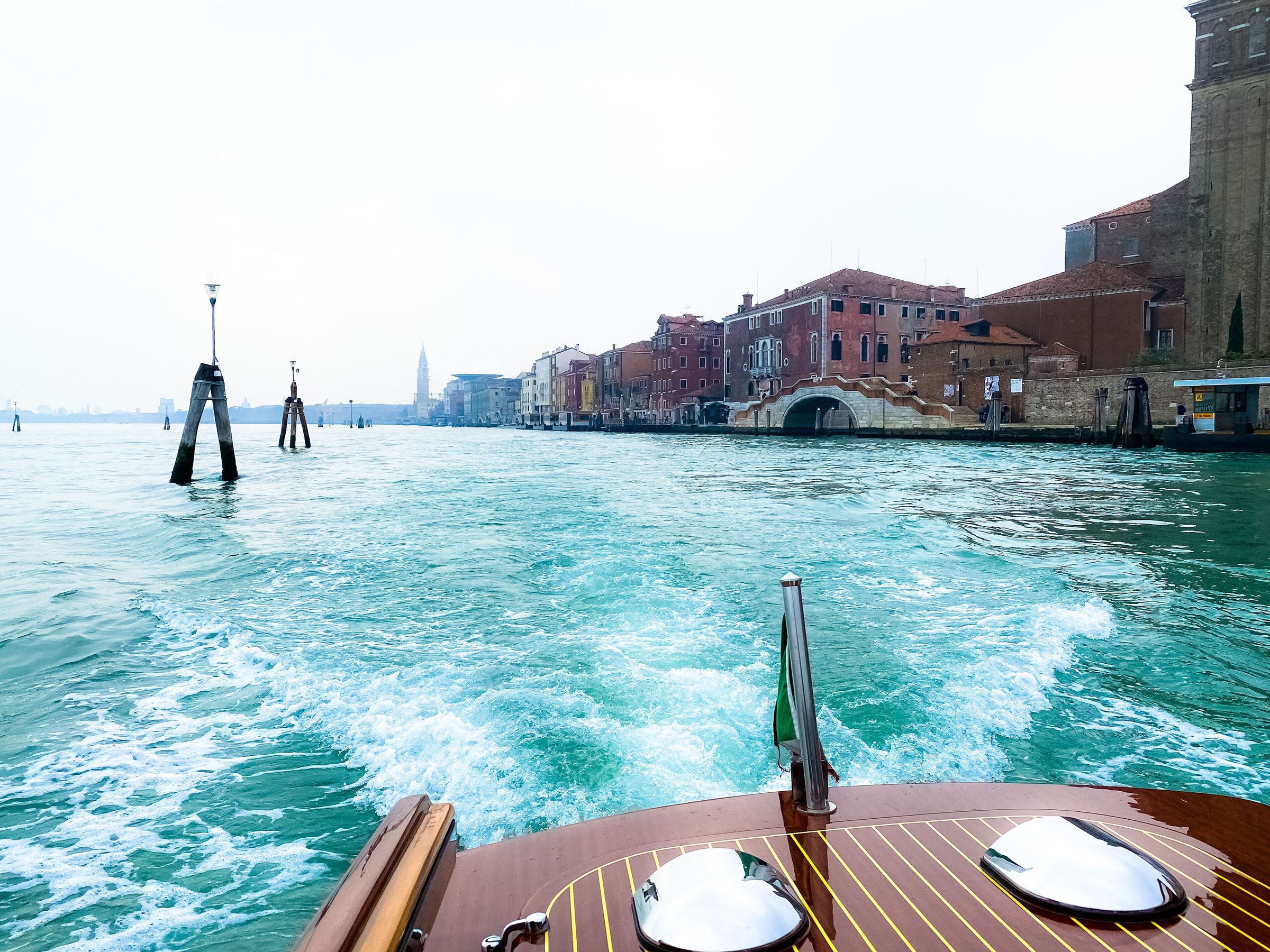Laguna Venice dilihat dari buritan boat taxi kayu yang meninggalkan kota, dengan buih air hijau toska.