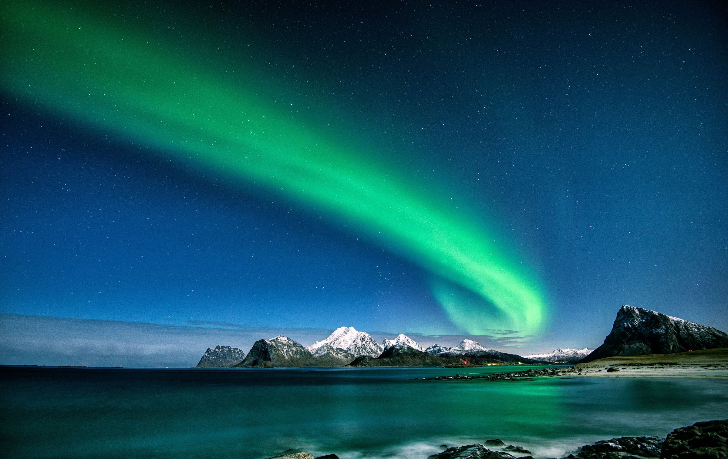 Aurora hijau melengkung di langit malam di atas pegunungan bersalju dan laut Lofoten Norwegia