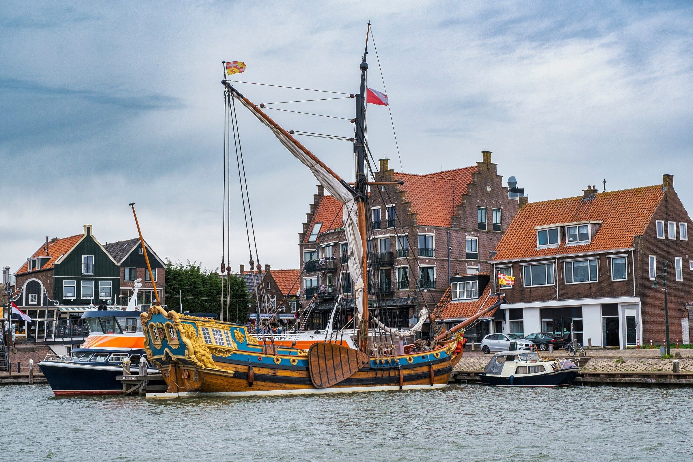 Kapal layar tua berhias di pelabuhan Volendam dengan rumah bata khas dan langit berawan.