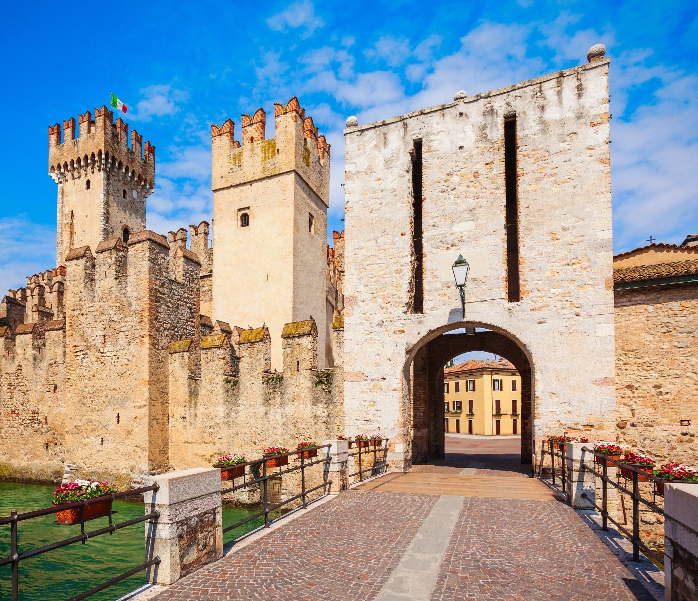 Gerbang dan jembatan masuk Kastil Scaligero di Sirmione dengan menara bata dan langit biru.