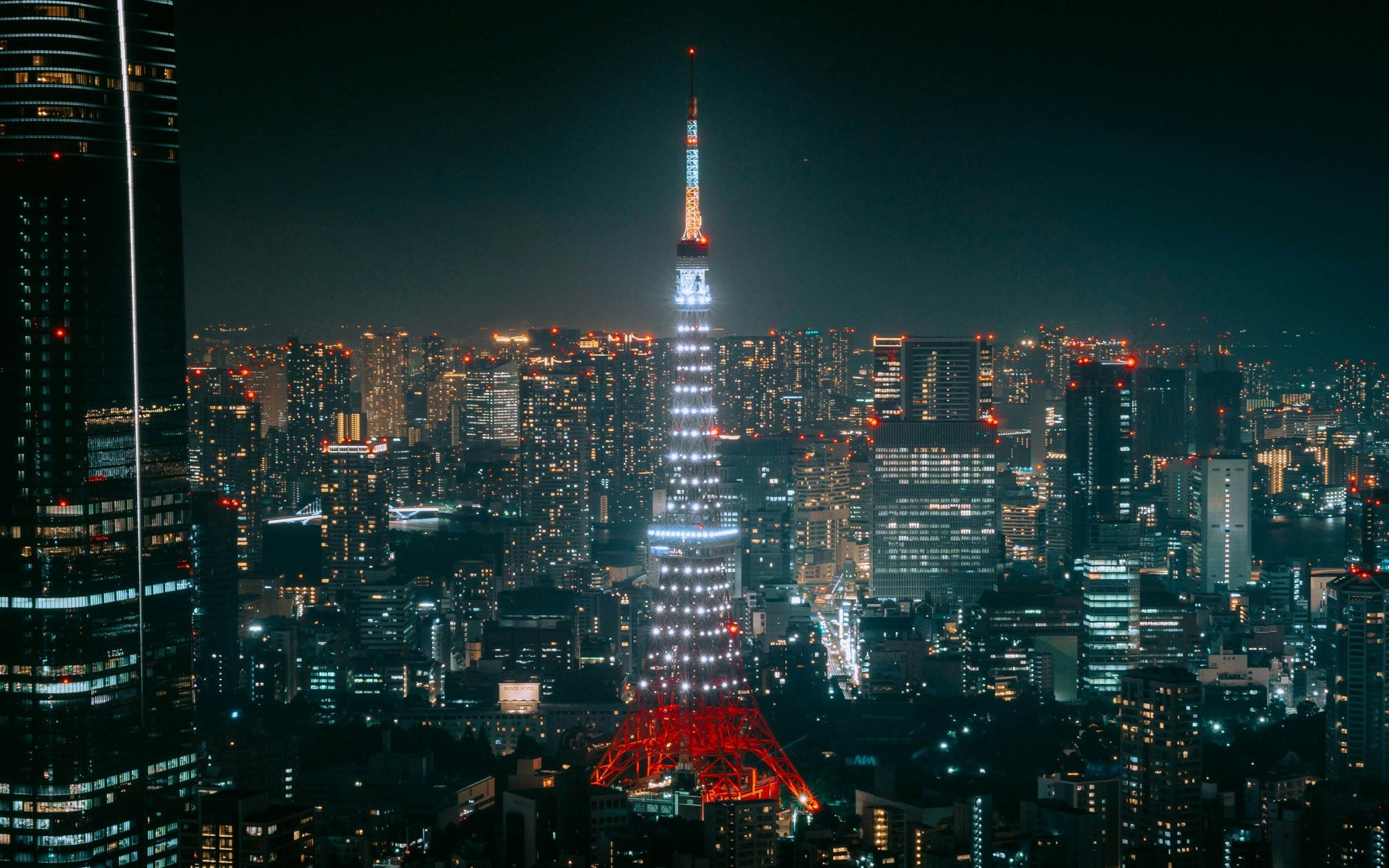 Tokyo Tower menyala merah-putih terang menjulang di tengah gemerlap gedung kota malam hari