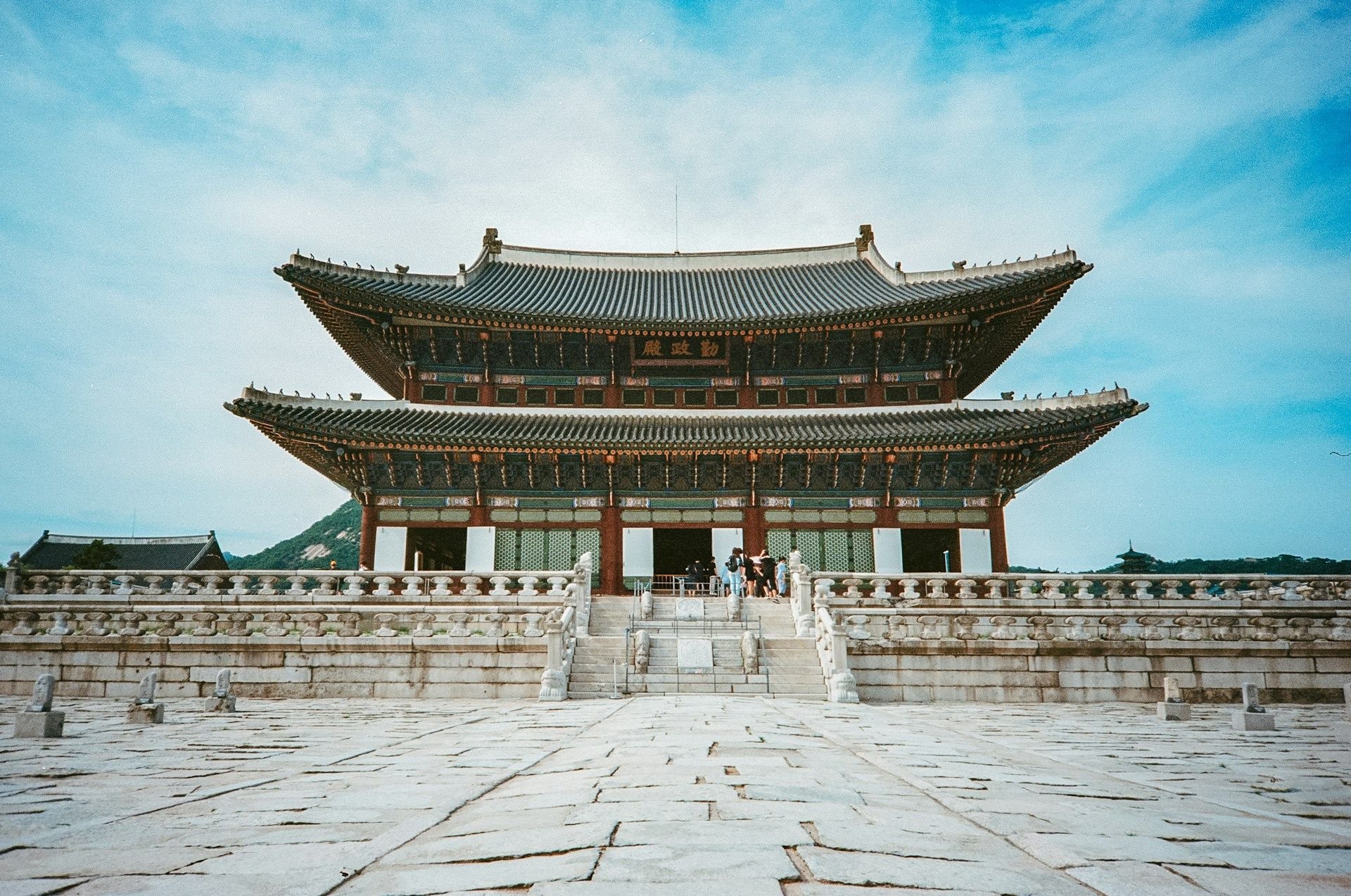 Halaman Istana Gyeongbokgung Seoul dengan atap kayu berwarna dancheong, paviliun tradisional, dan latar pegunungan musim gugur