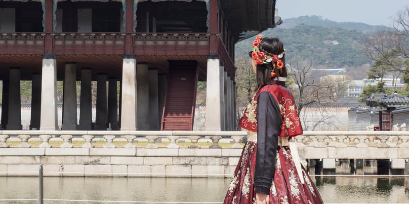 Perempuan berhanbok merah marun berdiri di tepi kolam depan paviliun Gyeonghoeru, Istana Gyeongbokgung Seoul