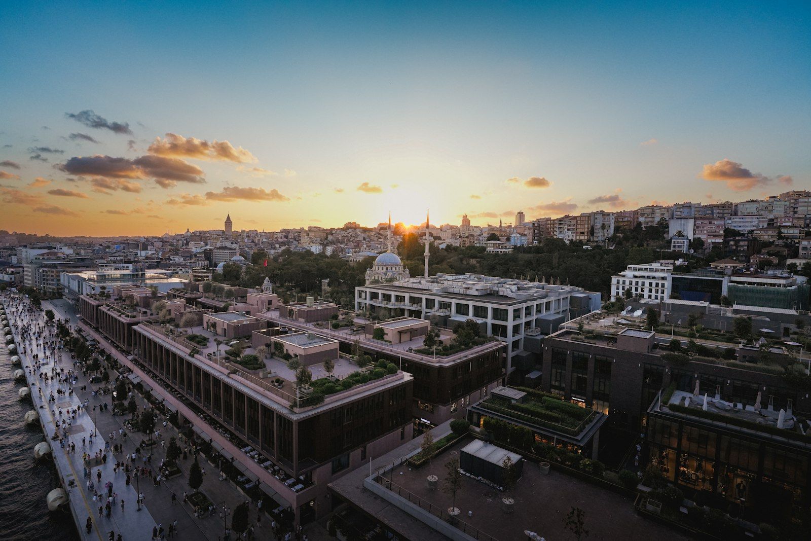 Pemandangan Istanbul saat senja dengan dermaga ramai, bangunan modern, masjid, dan Menara Galata.