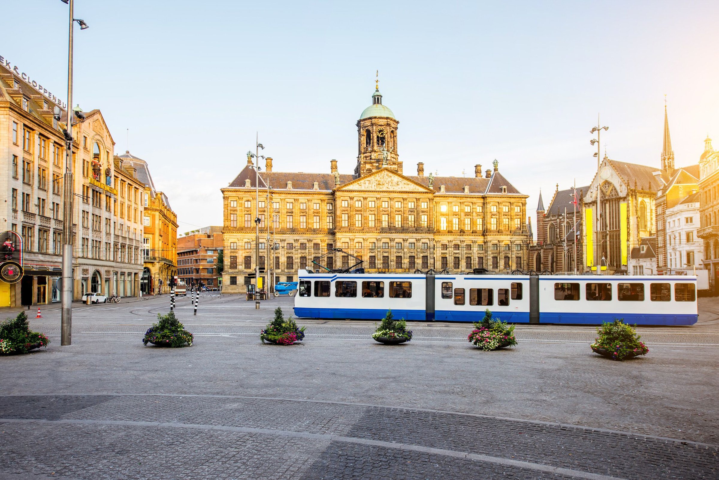Dam Square dan Royal Palace Amsterdam dengan trem biru melintas di pagi hari yang cerah.